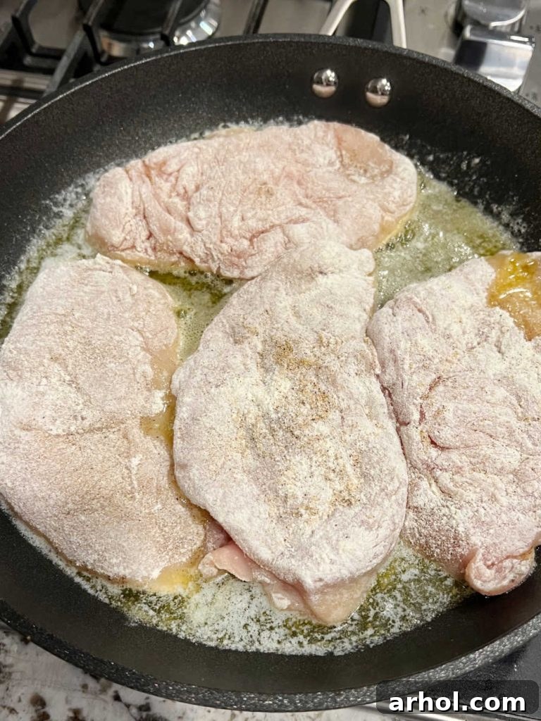Chicken cutlets cooking in a hot skillet, achieving a golden brown color.