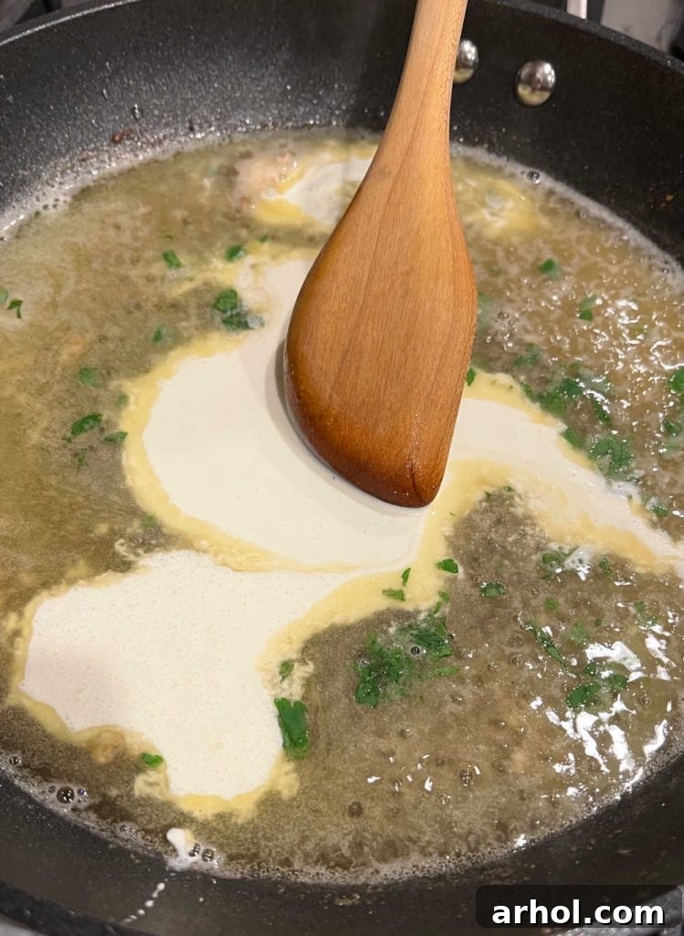 Stirring heavy cream into the lemon butter sauce with capers in a skillet.