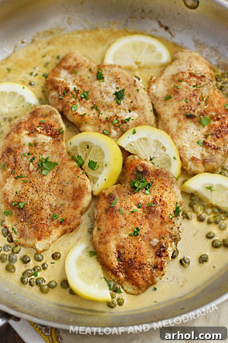 Pan-fried lemon chicken breasts in a creamy lemon caper sauce, garnished with fresh parsley and lemon slices in a skillet.