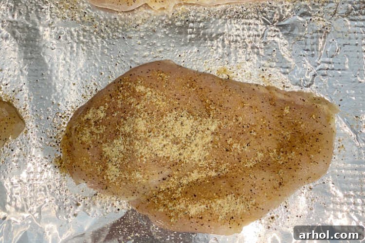 Seasoned chicken breasts arranged on a baking sheet lined with foil, ready for the oven.