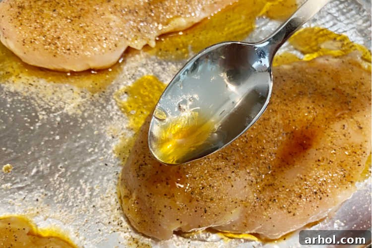 A spoon drizzling honey soy sauce mixture over chicken breasts on a baking sheet.