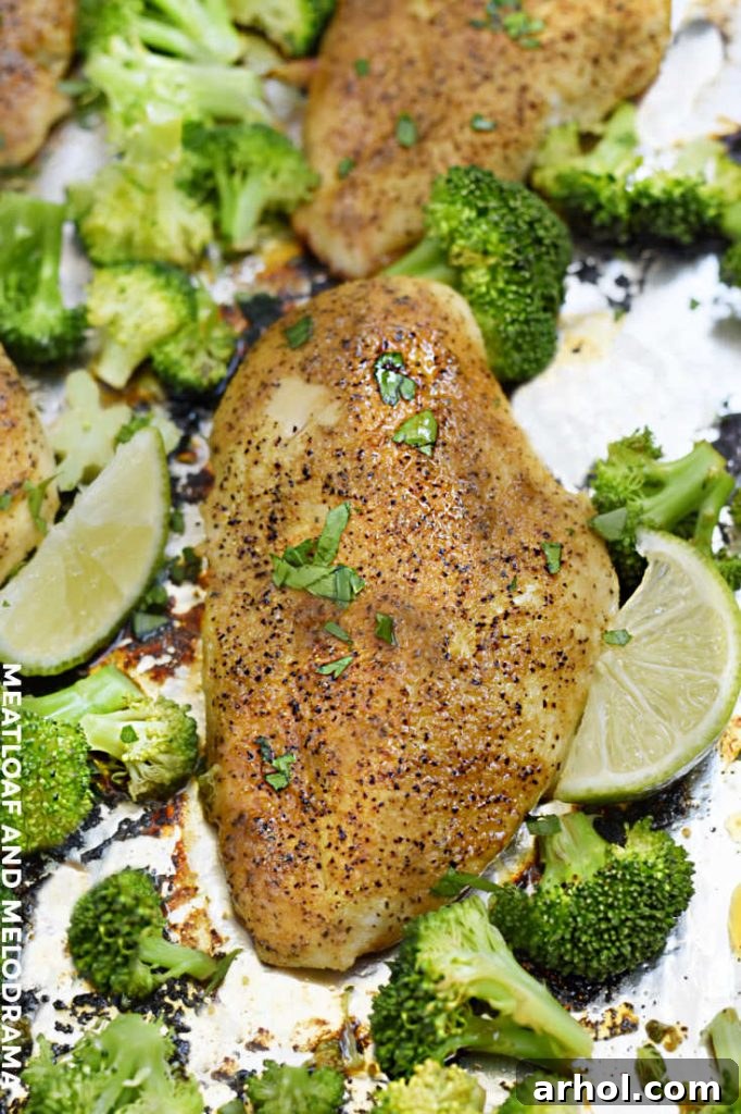 Baked honey lime chicken and broccoli served on a sheet pan with lime wedges.