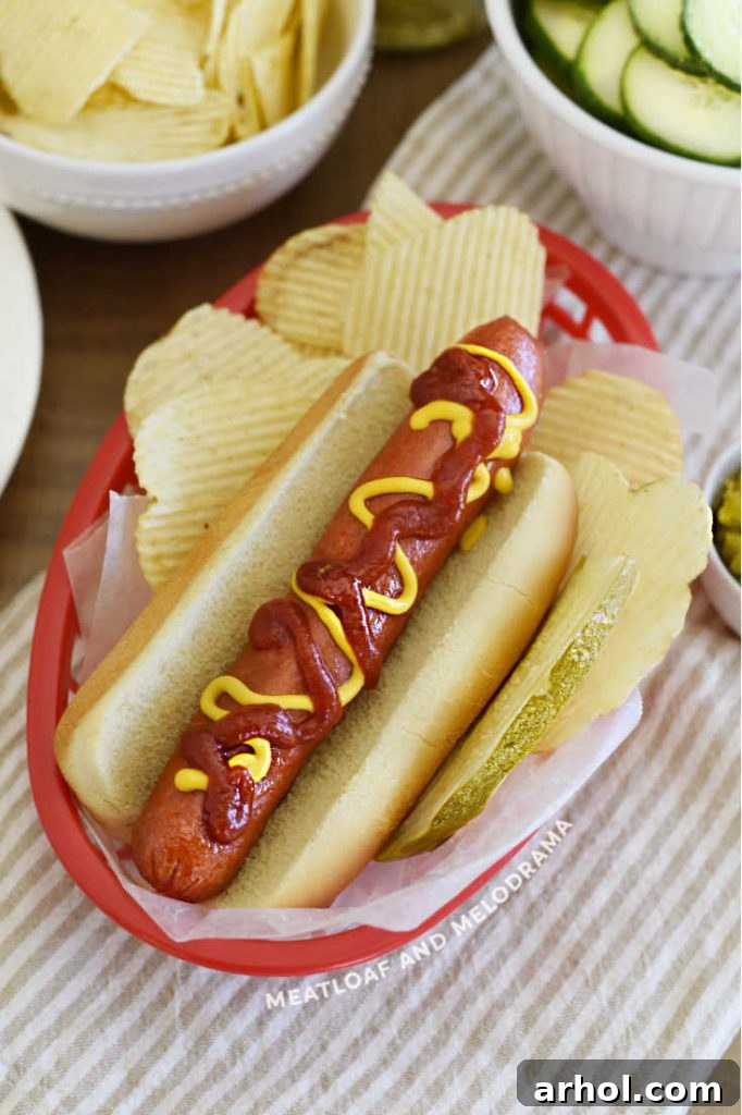 hot dog with mustard, ketchup, pickle and potato chips in red dish
