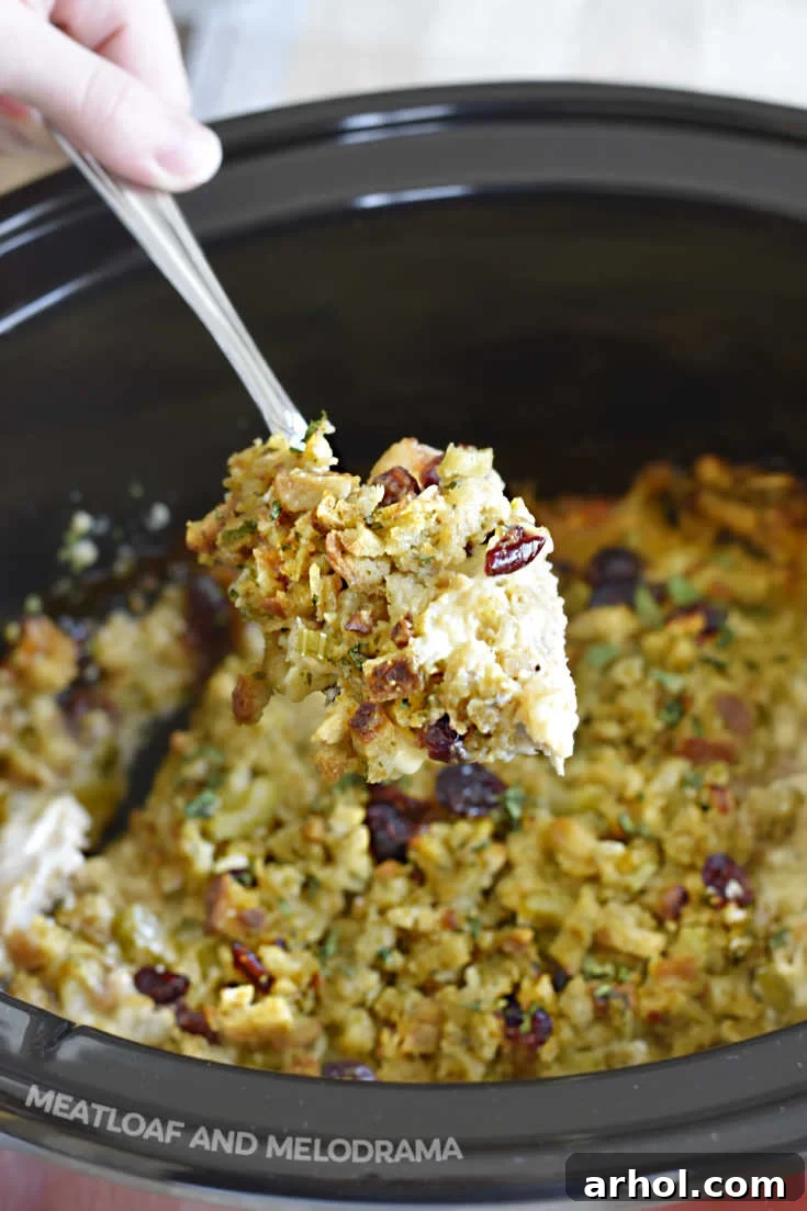 A serving spoon lifting a portion of cooked crockpot chicken and stuffing from the slow cooker