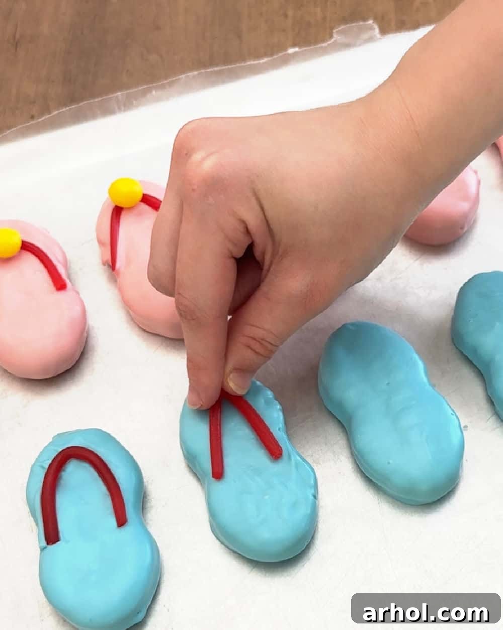 adding Twizzler strips to a coated cookie to form flip flop straps.