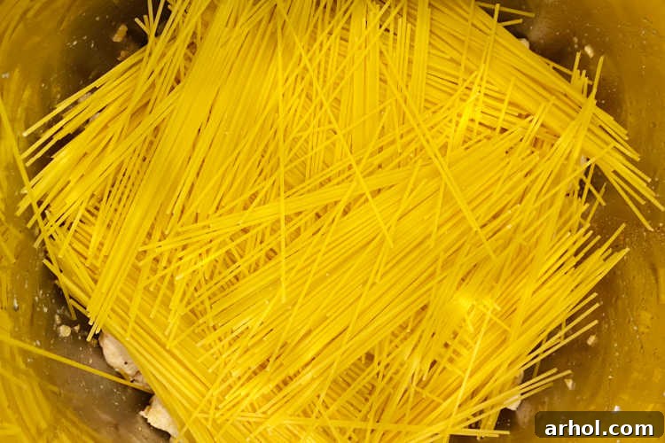 Creamy Instant Pot Chicken Spaghetti 4 Uncooked dry spaghetti noodles are neatly layered in a criss-cross pattern over chicken in an Instant Pot, ready for liquid and pressure cooking.