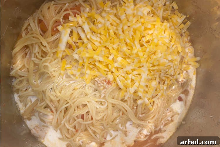 Creamy Instant Pot Chicken Spaghetti 6 Cream and cheese being stirred into cooked spaghetti and chicken in an Instant Pot, creating a rich and creamy sauce.
