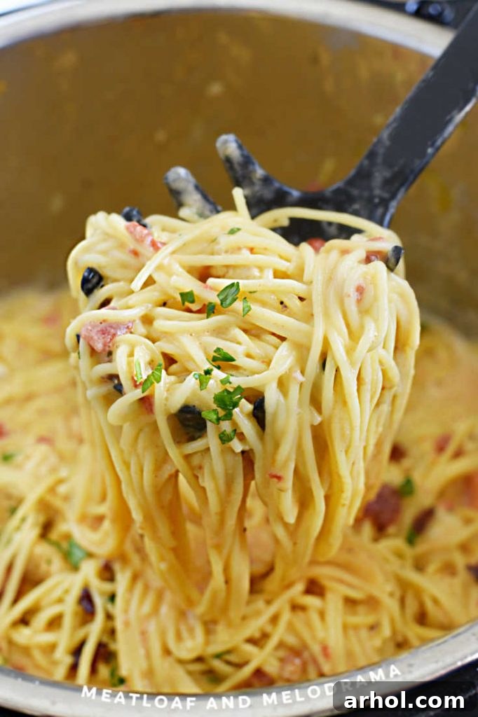 Creamy Instant Pot Chicken Spaghetti 7 A serving spoon lifting creamy Instant Pot chicken spaghetti from the pressure cooker, garnished with parsley and tomatoes, with bacon visible.