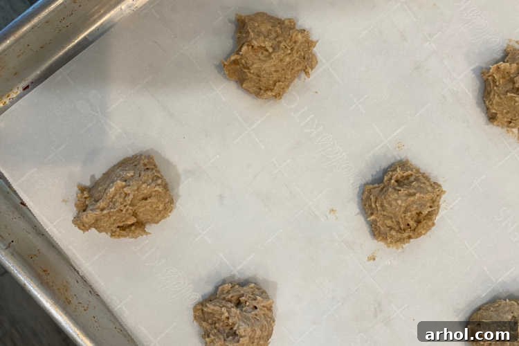 Scoops of unbaked banana oatmeal cookie dough with chocolate chips neatly arranged on a parchment-lined baking sheet, ready for the oven