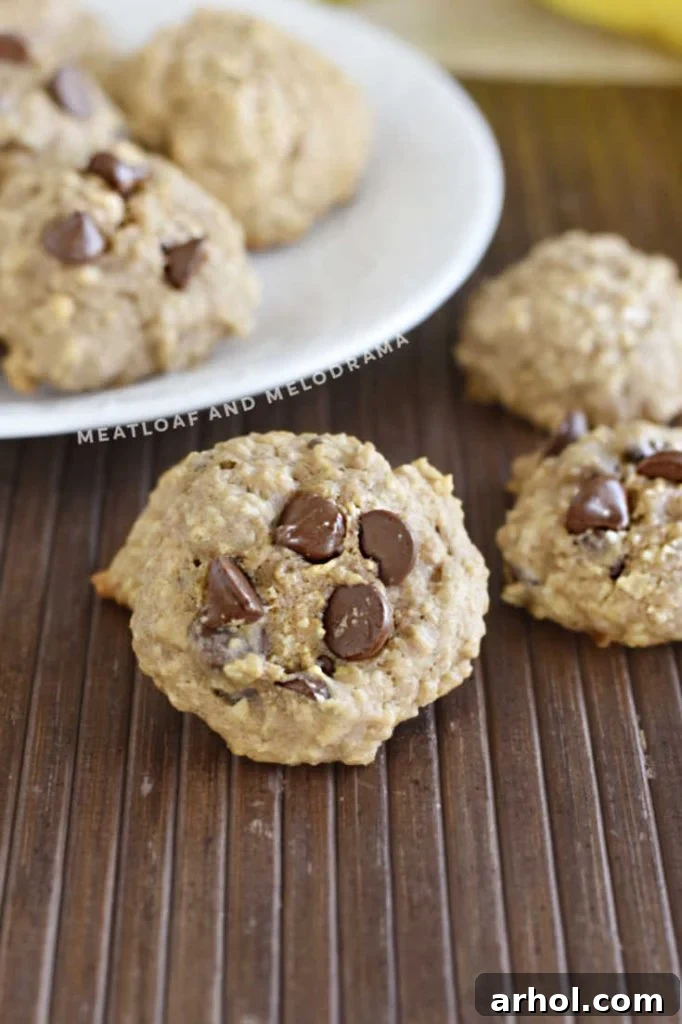 Two plates of freshly baked banana oatmeal chocolate chip cookies, one stacked and the other with scattered cookies, presented on a light-colored kitchen table