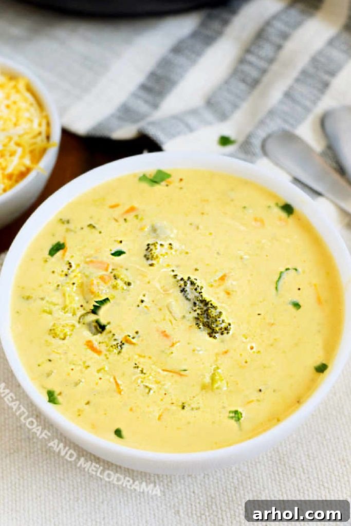 Velvety Instant Pot Broccoli Cheddar Soup 2 A steaming white bowl filled with creamy Instant Pot Broccoli Cheddar Soup, garnished with a sprinkle of fresh parsley. The rich, golden-orange hue indicates the generous presence of cheddar cheese, while visible tender broccoli florets and shredded carrots add texture and visual appeal. The soup looks inviting and hearty.
