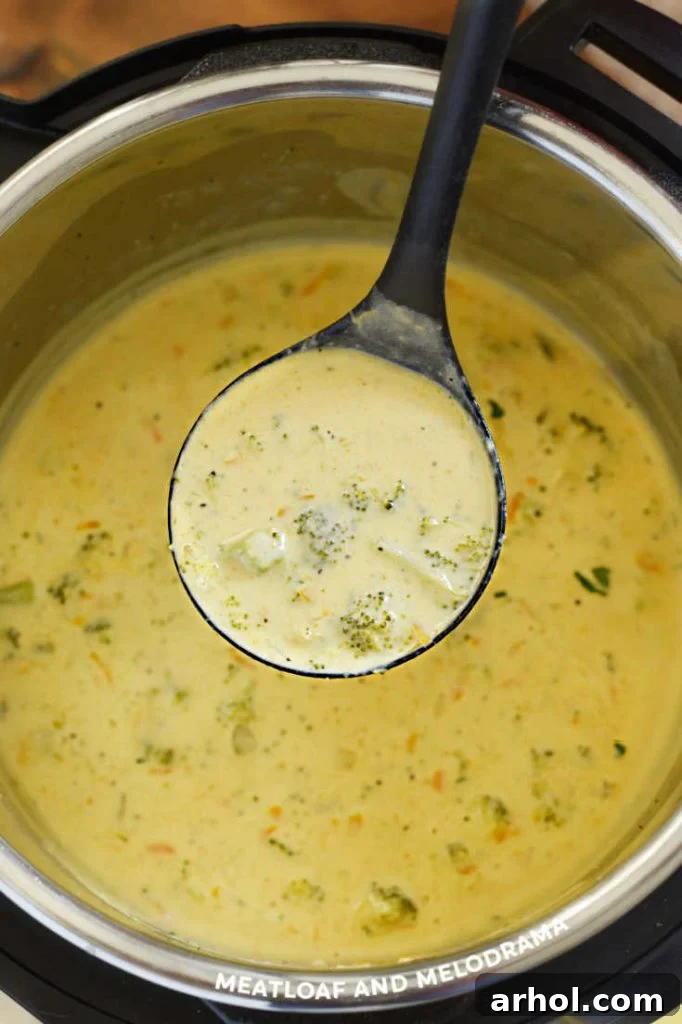 Velvety Instant Pot Broccoli Cheddar Soup 6 A metallic ladle brimming with thick, creamy Instant Pot Broccoli Cheese Soup is held just above the open Instant Pot. The soup appears rich with melted cheddar cheese and tender broccoli pieces, showcasing its ready-to-serve appeal and hearty texture.