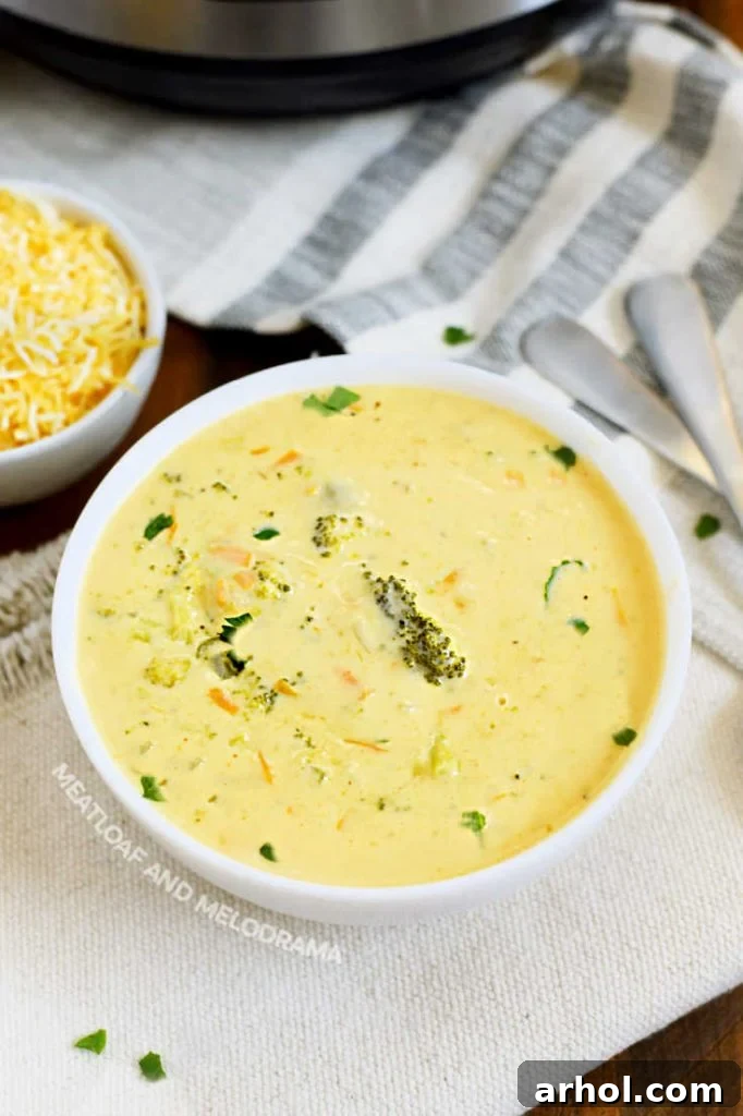 Velvety Instant Pot Broccoli Cheddar Soup 7 A white ceramic bowl filled to the brim with creamy Instant Pot Broccoli Cheddar Cheese Soup. A small side dish holds extra shredded cheddar cheese for garnish, and a sprig of fresh herb provides a final decorative touch. The setting evokes a cozy, comforting meal.