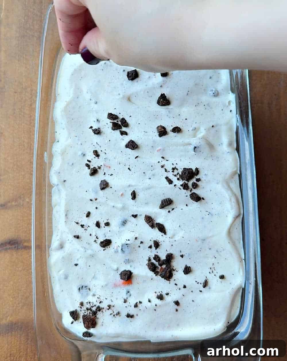 Adding more cookie crumbs and sprinkles to the top of the ice cream mixture in a loaf pan.