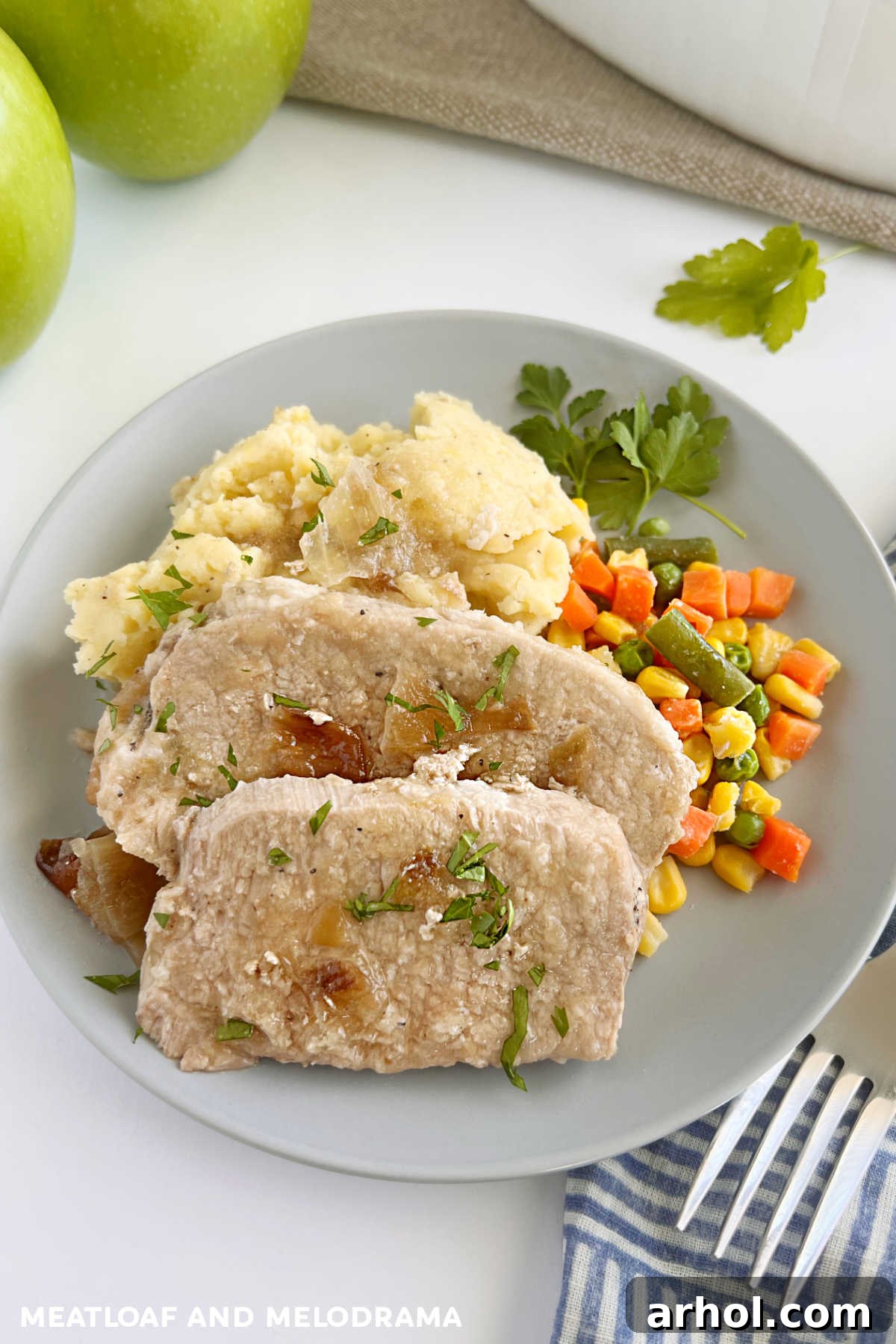 A serving of slow cooker pork roast with apples and onions, accompanied by creamy mashed potatoes and vibrant green vegetables, on a dinner plate.