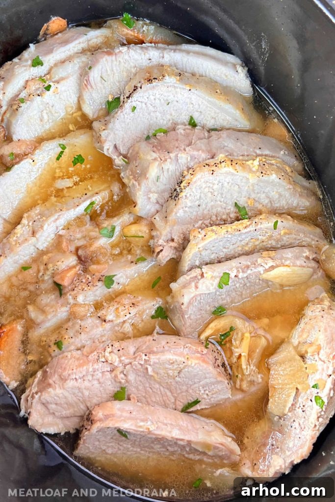 Close-up of juicy, thinly sliced slow cooker pork roast resting in its own delicious juices within the slow cooker, ready to be served.
