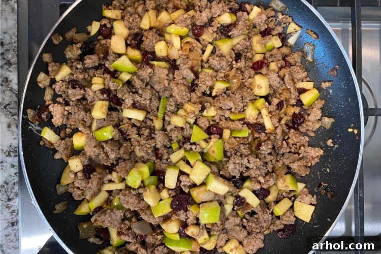 Sautéed Italian sausage with apple cubes and dried cranberries in a skillet