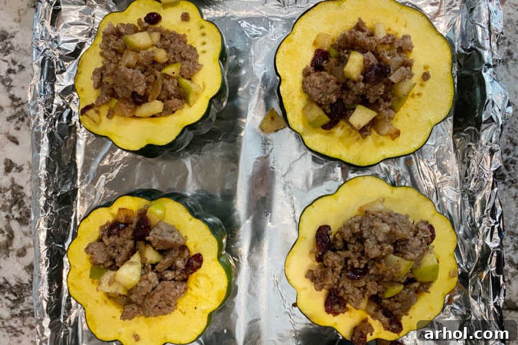 Acorn squash halves generously stuffed with sausage, apples, and cranberries on a foil-lined baking sheet