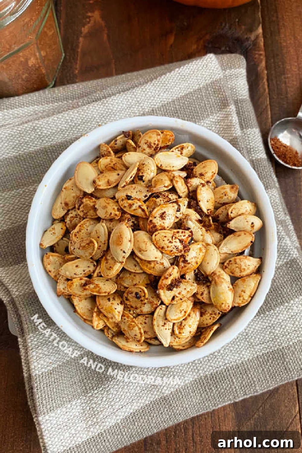 Seasoned roasted pumpkin seeds in a white bowl on a wooden table, ready to be enjoyed.