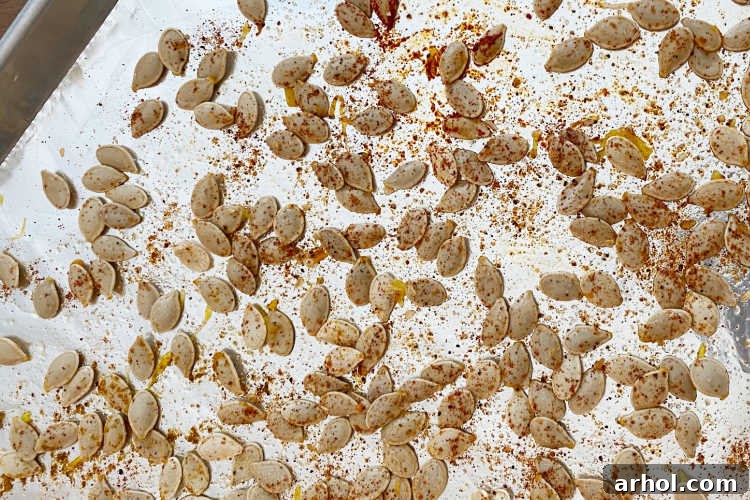 Cleaned and seasoned pumpkin seeds spread in a single layer on a baking sheet, ready for roasting.