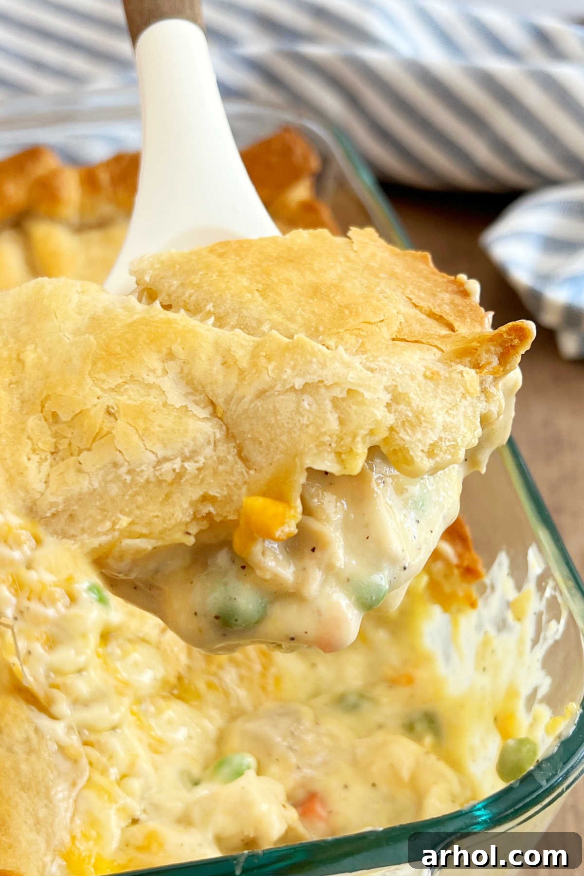 A delicious serving of chicken pot pie with a golden crescent roll crust, scooped onto a serving spoon.