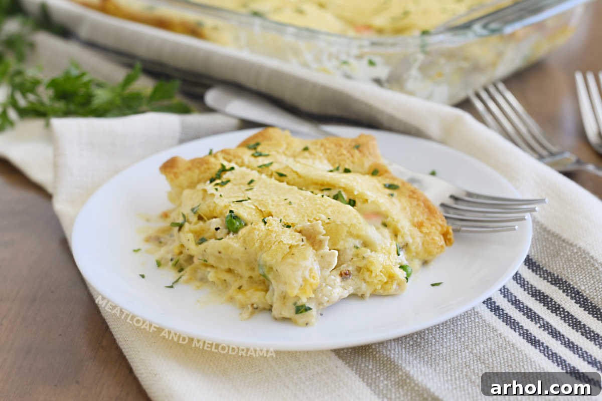 A large serving of chicken pot pie with a golden, flaky crescent roll crust on a white plate, ready to be enjoyed.