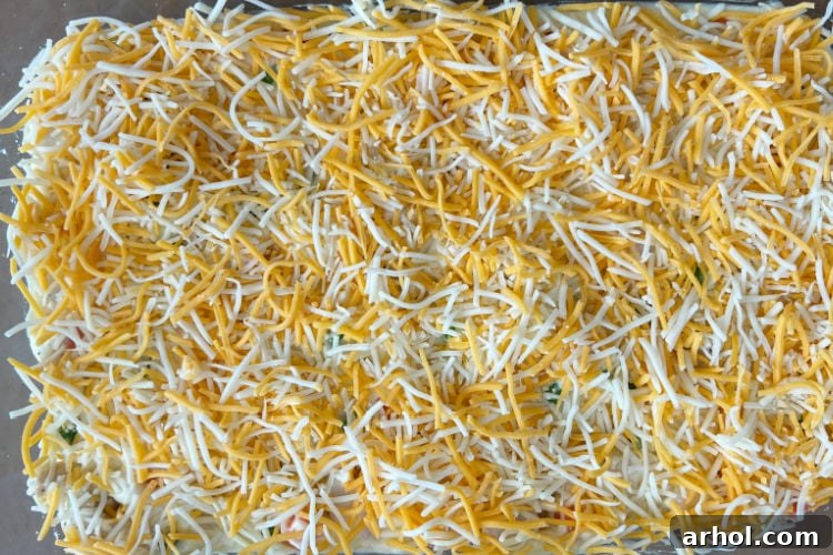 A generous layer of shredded cheddar blend cheese topping the chicken casserole filling.
