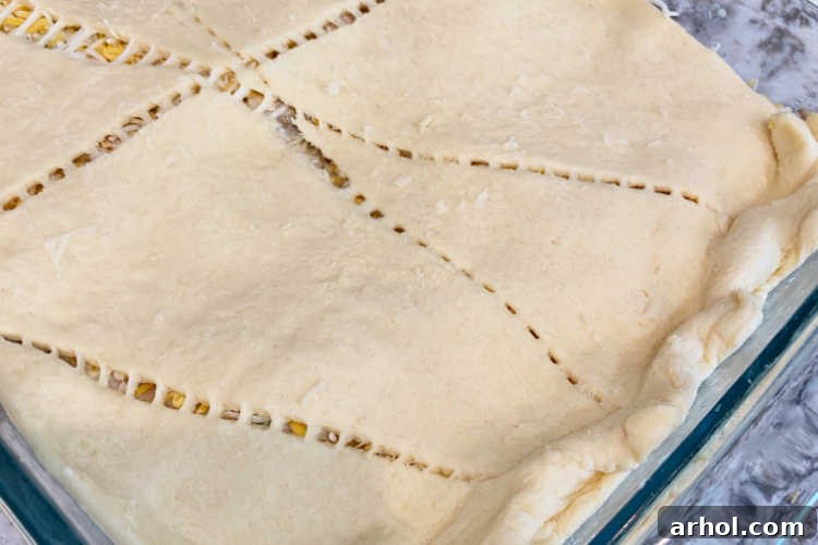 A sheet of crescent roll dough carefully placed on top of the chicken casserole mixture in a baking dish.