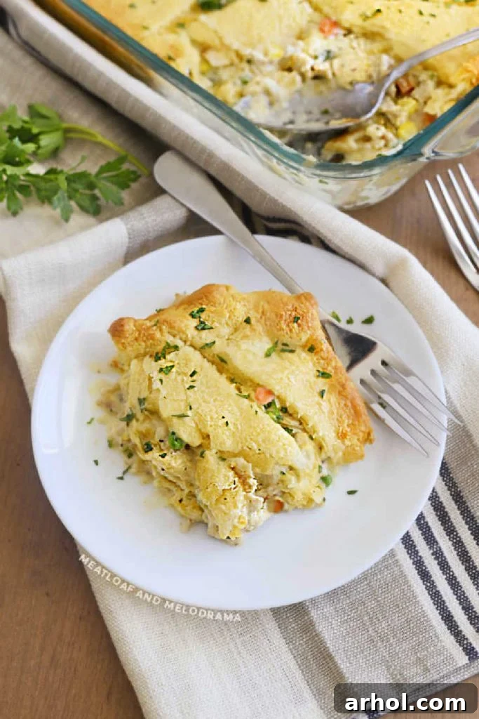 A slice of chicken pot pie with a golden crescent rolls crust, served on a white plate.