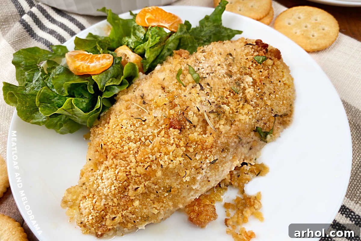 A baked Ritz Cracker Chicken breast served on a white plate with a fresh green salad, highlighting its crispy, golden crust.