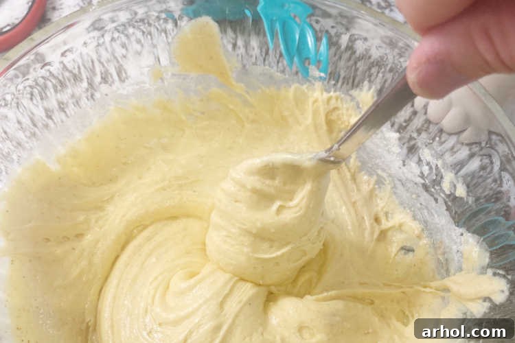 Festive Baked Eggnog Donuts 3 Two key ingredients, eggnog and cake mix, are being expertly combined in a large bowl, forming a thick, smooth batter for homemade baked donuts.