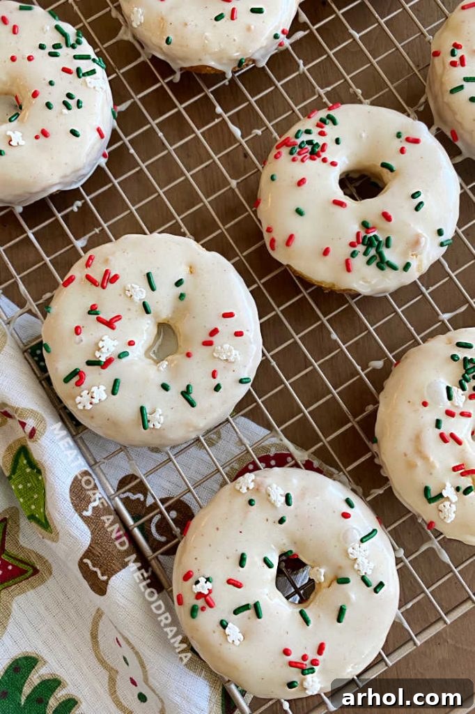 Festive Baked Eggnog Donuts 5 Freshly glazed eggnog donuts, vibrant with red and green holiday sprinkles, are cooling on a wire rack, showcasing a beautiful, irresistible finish.