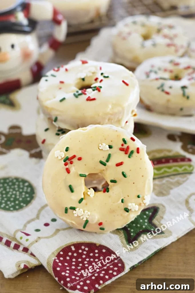 Festive Baked Eggnog Donuts 6 Beautifully glazed eggnog donuts with a generous scattering of red and green holiday sprinkles are artfully arranged on a festive table setting.