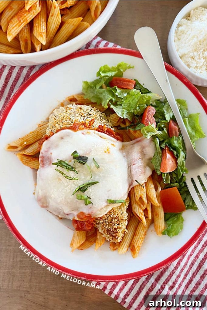 Baked panko-coated chicken breast topped with marinara sauce and melted cheese, served with penne pasta and a side salad on a plate.