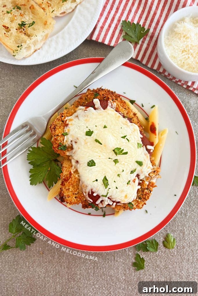 Baked chicken Parmesan breast with melted cheese and fresh basil on a rustic wooden table.