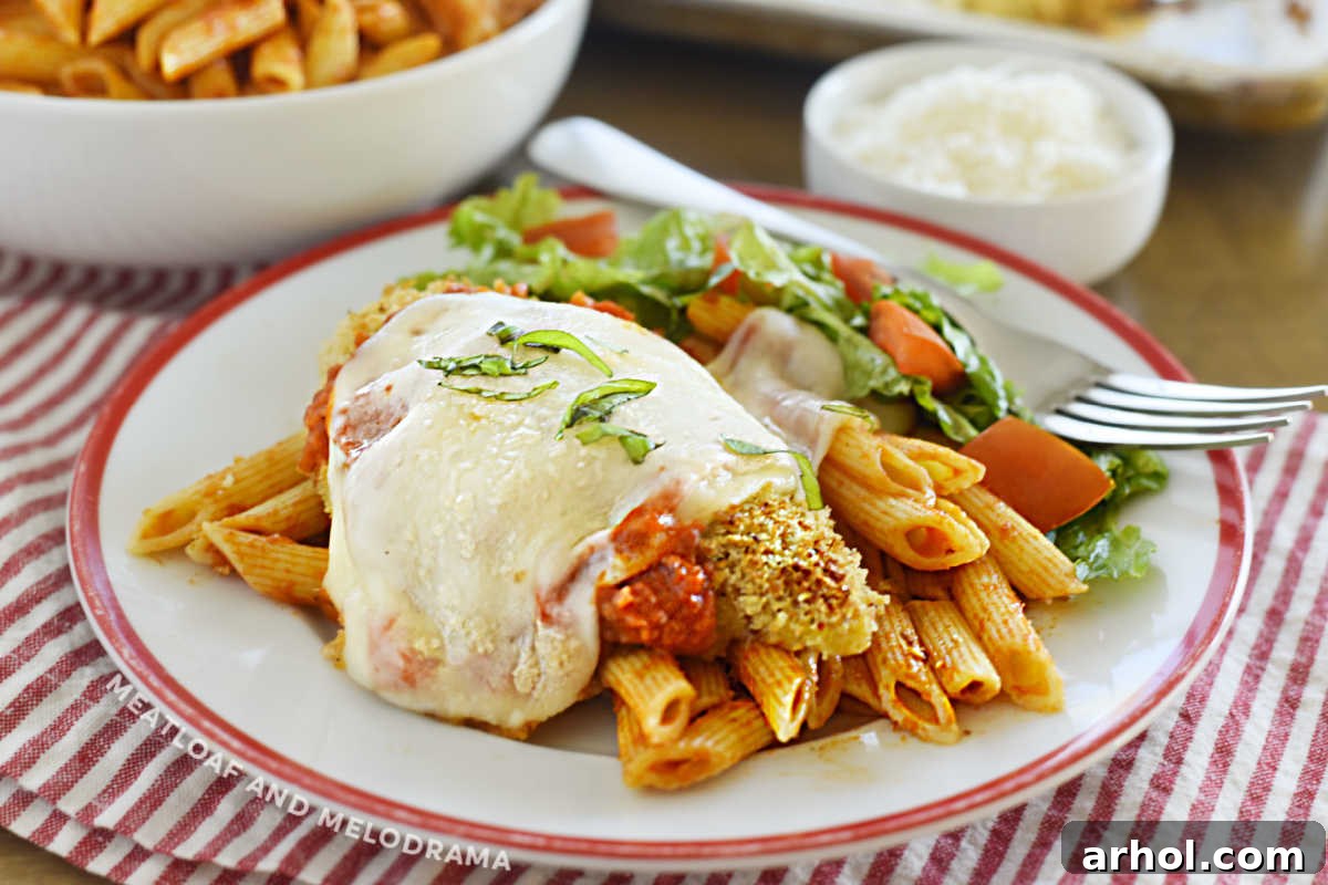 Close-up of baked chicken parmesan served over penne pasta on a white plate, ready to eat.