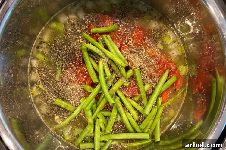 Minestrone soup ingredients, including canned beans, diced tomatoes, broth, and fresh green beans, layered in the Instant Pot before pressure cooking.