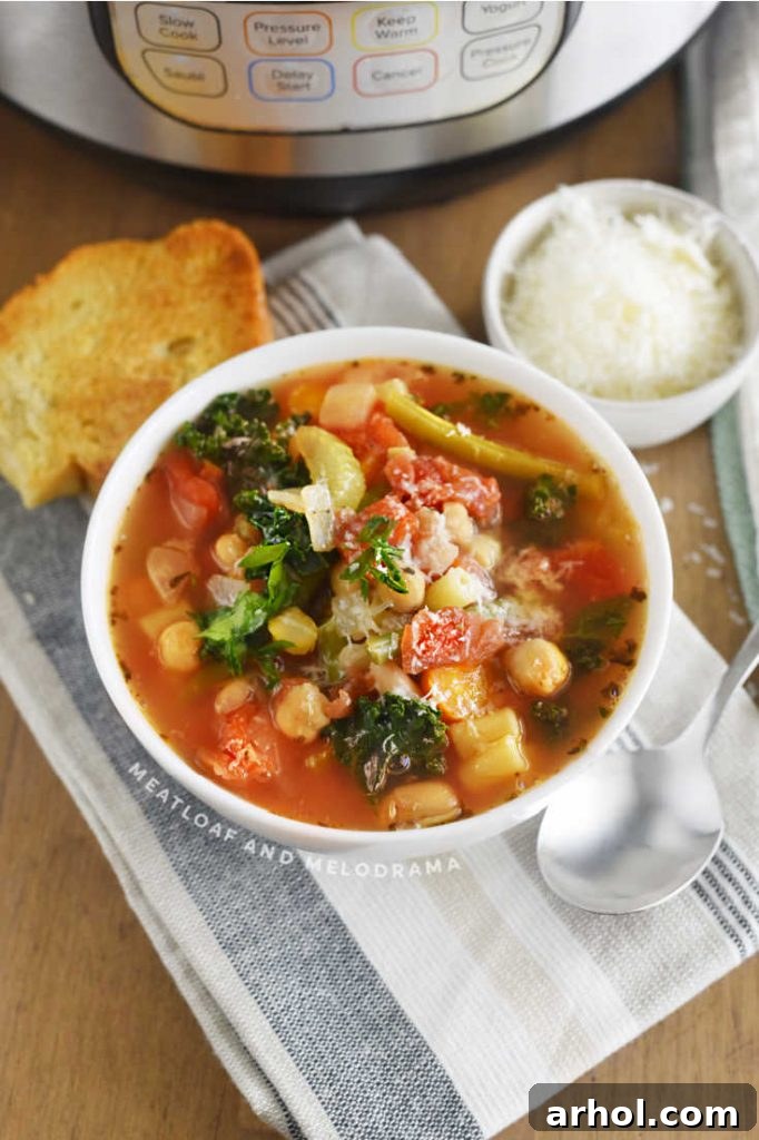 A close-up of a bowl of pressure cooker minestrone soup, featuring diced tomatoes, vibrant kale, hearty garbanzo and cannellini beans, and tender green beans.