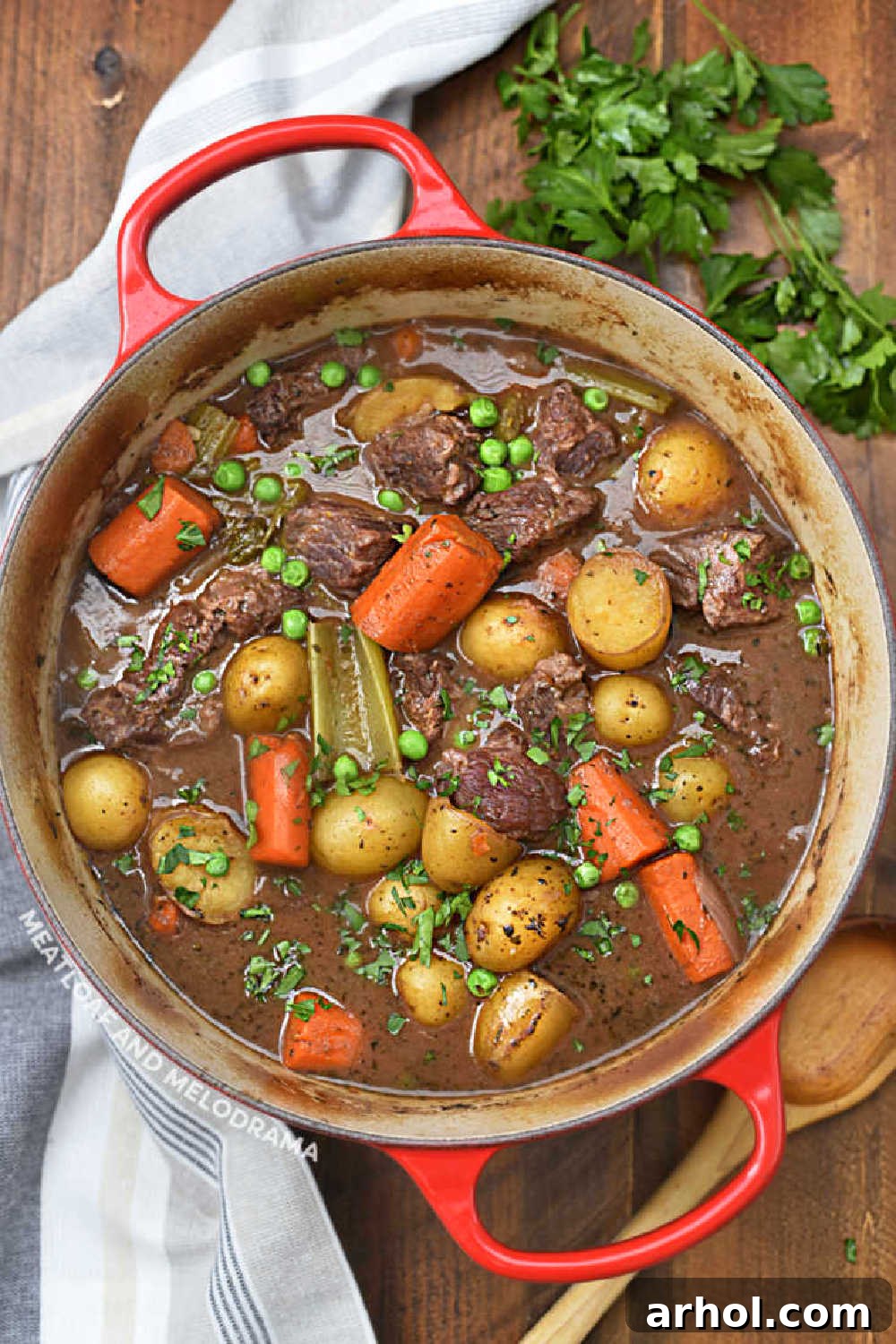 Hearty beef stew simmering in a vibrant red Le Creuset Dutch oven, filled with succulent beef chunks, carrots, and baby potatoes