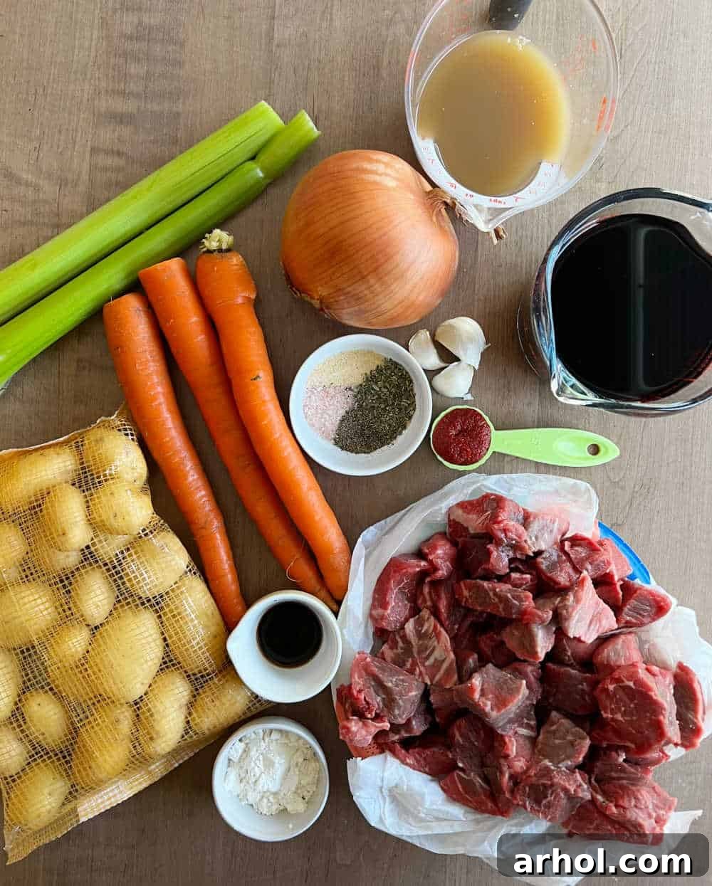 Assortment of fresh ingredients laid out for beef stew, including beef chunks, carrots, potatoes, and herbs
