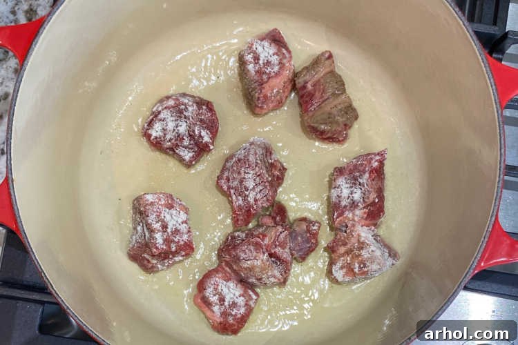 Close-up of beef chuck pieces browning in a Dutch oven, creating a rich, caramelized crust