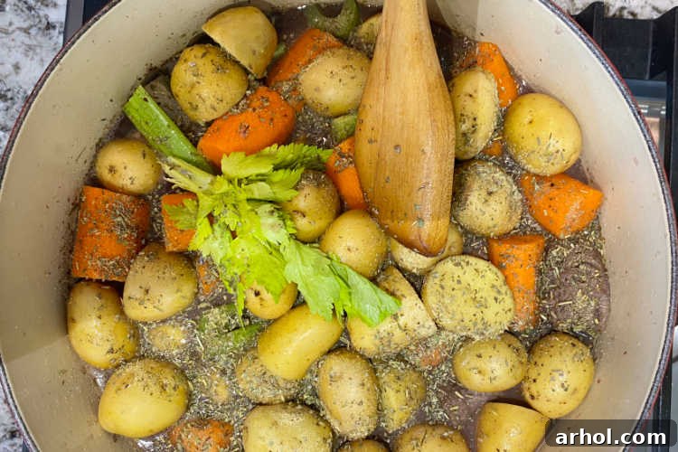 A Dutch oven filled with beef chunks, potatoes, carrots, and celery, ready for slow cooking