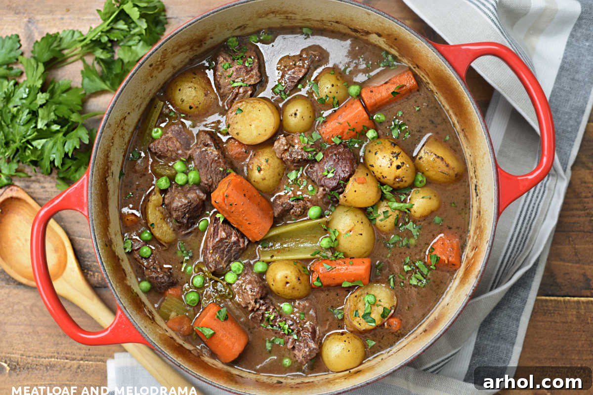 Hearty beef stew with carrots, potatoes, peas, and celery in a red Dutch oven, garnished with fresh herbs