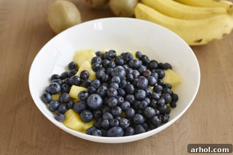 Close-up shot of fresh blueberries and perfectly cubed pineapple chunks waiting in a white bowl, ready to be combined with other fruits for the salad.