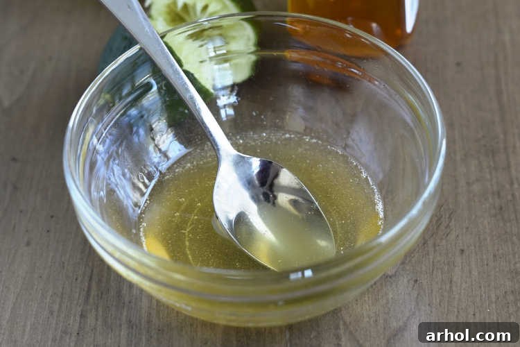 A small glass mixing bowl holding the freshly prepared honey lime dressing, featuring the vibrant yellow of lime juice and the golden hue of honey, ready to be poured over the fruit.