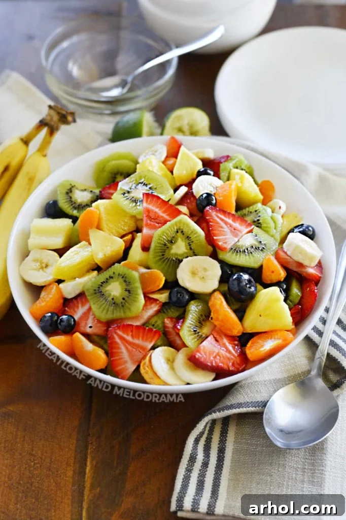 A delightful mix of various cut-up summer fruits, including kiwi, pineapple, blueberries, strawberries, mandarin oranges, and bananas, presented vibrantly in a crisp white bowl.