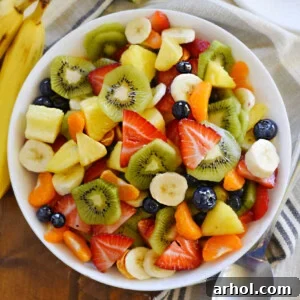 A bowl of vibrant tropical fruit salad featuring mandarin oranges, ripe bananas, and fresh pineapple chunks, all glistening and ready to serve, representing the deliciousness of this recipe.
