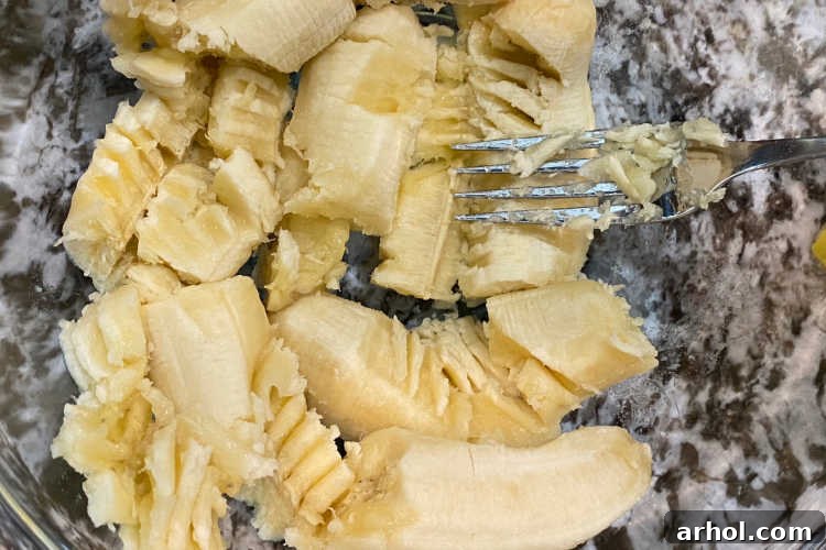 Mashing ripe bananas in a mixing bowl with a fork, ready for the cake mix