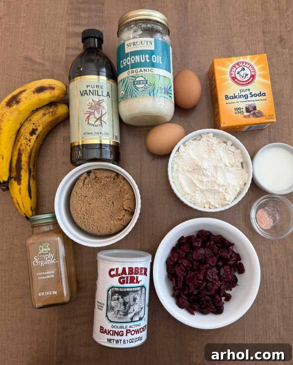 Sweet and Tart Banana Cranberry Muffins 3 A flat lay photograph displaying the key ingredients for banana cranberry muffins: ripe bananas, a bowl of vivid red dried cranberries (Craisins), flour, eggs, and other essential baking components.