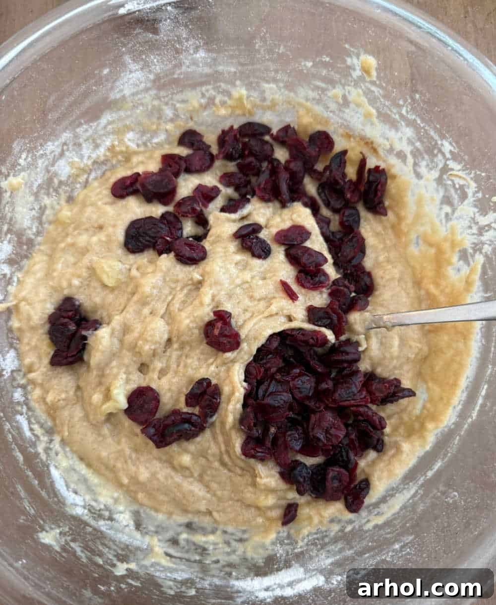 Sweet and Tart Banana Cranberry Muffins 6 A large mixing bowl containing the banana muffin batter, with vibrant red dried cranberries being folded in, ensuring even distribution throughout the mixture.